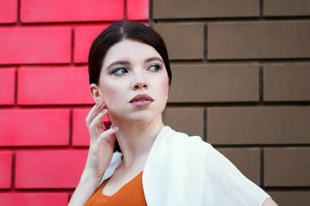 Lovely girl posing by red-brown brick wall. Young caucasian attractive brunette woman looking at...