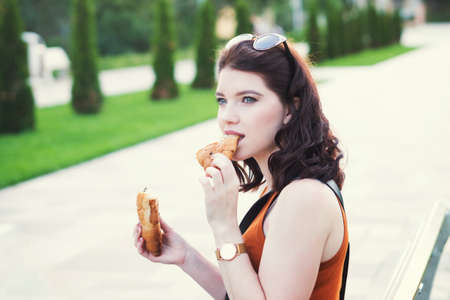 Cute charming girl has snack of croissant while walking in summer park. Summer time. Freedom.
