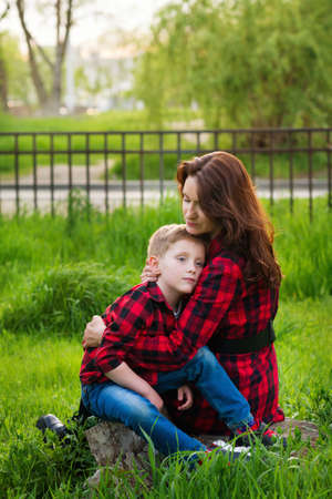Little boy lies on mothers shoulder in nature background. Mommy embracing and consoles her kid son...