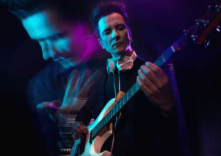 Handsome male musician with electric guitar in recording studio. Guitarist performance. Guitar player strumming. Rock music concept. Multiple exposure neon atmosphere on background.の写真素材