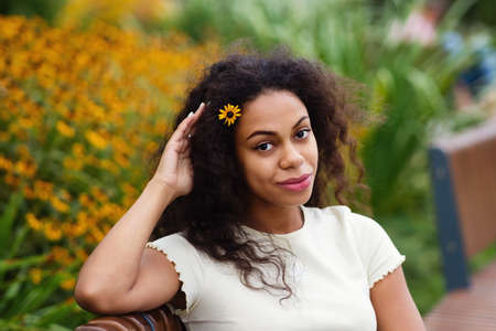Portrait of African American Young Woman with yellow flower on nature background. Dark skinned brunette Female with loose wavy curls african american hair. Hipster Mixed Race Girl. Soft focus.の写真素材