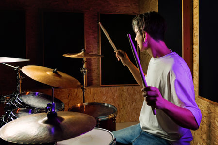 Drummer playing drums while sitting at drum kit with colorful backlit on background. Rock musician playing on drum kit indoor. Music, People, Musical Instruments and Entertainment Conceptの写真素材