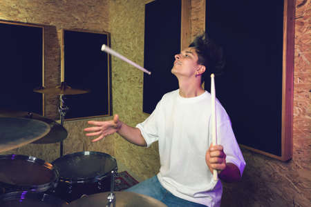 Musician artist beating rhythm is rehearsing behind drum kit in recording studio. Emotional Handsome male drummer hitting percussion instrument. Music and Entertainment Conceptの写真素材