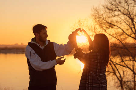 Silhouettes of lovers at sunset by lake spend time sweating outdoors. Sun is reflected in water....