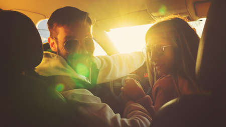 Happy family traveling by car on sunny day. Couple is looking at camera and smiling sitting in car....