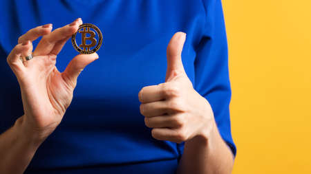 Faceless girl holds golden physical bitcoin and shows Okay sign, thumbs up, ok gesture. Female Hand...