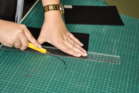 Hands of woman using sharp knife when cutting black paper for making notebook with interchangeable blocks on rings, hand-assembledの写真素材