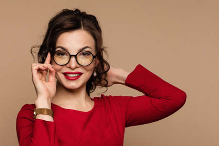 Elegant smiling female in round eyeglasses on beige background. Beauty portrait gorgeous woman in...