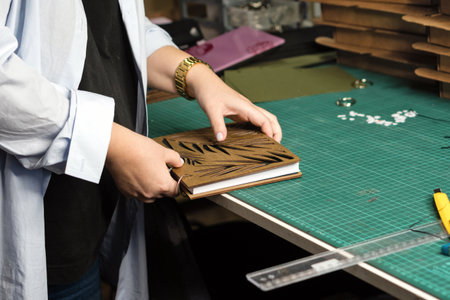Female hands hold notebook with removable blocks and wooden cover together in workshop. Craft...