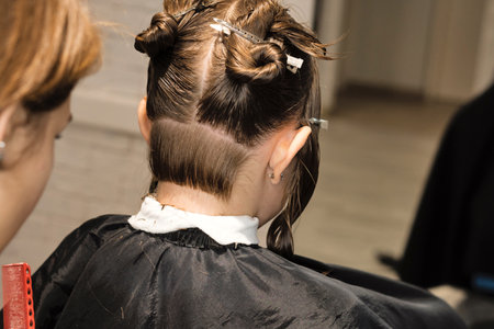 Hand of hairdresser doing haircut of kid with hair clips on her hair in salon. Hairtician cuts wet hair of child combing with comb. Little Girl Client with Short Bob Hair. Close Up Back Viewの写真素材