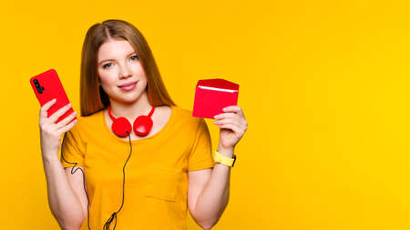 Girl in basic yellow outfit hands holding red paper envelope, cell phone, headphone on yellow wall. Online mail, correspondence, feedback, reporting. Greeting card. New mail, message. Postal service.の写真素材
