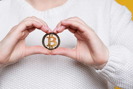 Faceless woman in white sweater holding golden bitcoin, advertise of digital money btc coin for...