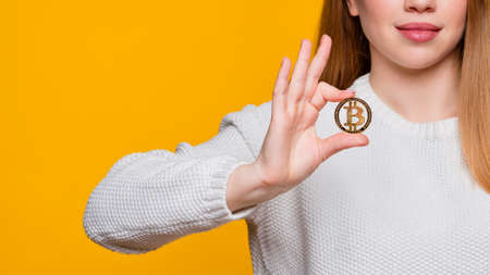 Faceless woman in white sweater holding golden bitcoin, advertise of digital money btc coin for e-commerce. Hands unrecognizable girl hold golden bitcoin. Cryptocurrency, blockchain, tokens and nft.の写真素材
