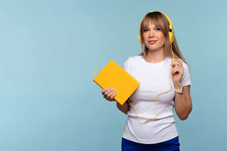 Pretty young woman holds book on light blue background. Empty work area Listen to audiobooks...
