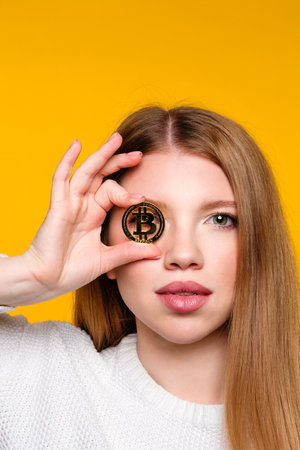 Cryptocurrency and blockchain. Girl shows btc coin holding in front of eye. Woman holding golden...