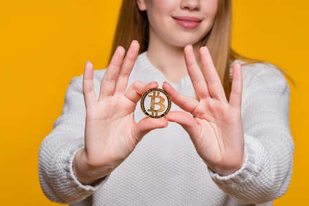 Faceless woman in white sweater holding golden bitcoin, advertise of digital money btc coin for...