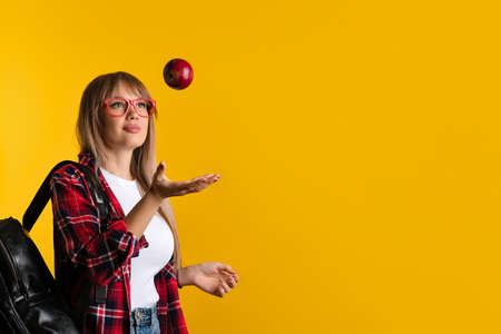 Girl student wears casual clothes and red eyewear. Smart Young woman juggling with red apple on yellow background. Healthy eating and healthy snacking during college concept.の写真素材