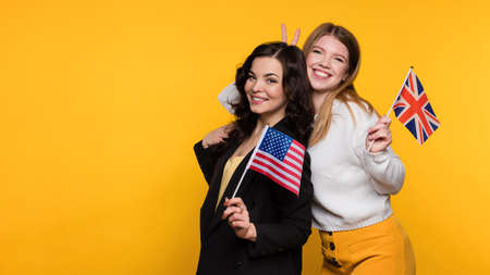Two Young Women Hug, Have Positive Emotions and Holding Flags UK and USA. Study Abroad. International Student Exchange Program. Foreign language courses. British English and American English.の写真素材