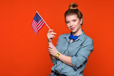 Smiling woman holds small american flag. Female student recommending foreign language studying school. Learning American English, student exchange and travel conceptの写真素材