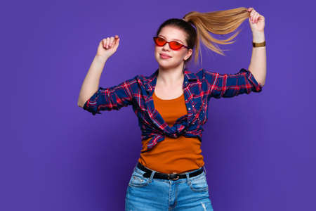 Young woman in stylish hat and warm burgundy sweater on blue background in studio. playful girl...