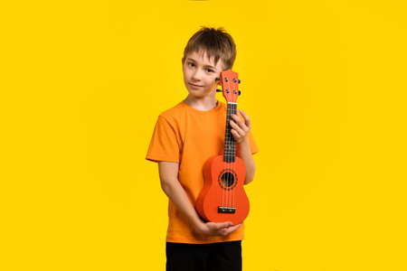 Child play acoustic Ukulele guitar on yellow background. Hawaiian small guitar. Concept of Music Education and Training Practice in Music Schoolの写真素材