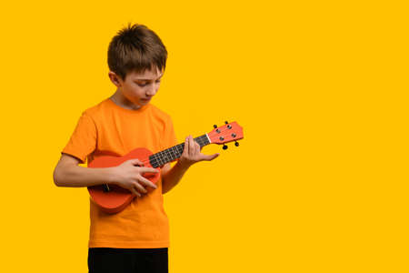 Child play acoustic Ukulele guitar on yellow background. Hawaiian small guitar. Concept of Music Education and Training Practice in Music Schoolの写真素材