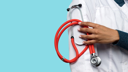 Unrecognizable dark skinned female doctor close up with medical stethoscope on blue background in...