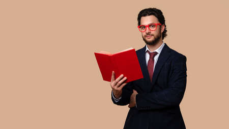 Handsome Bearded Man Wears Suit Tie and Red Eyewear Hold Book and Look at Camera on Pastel Background. wide banner. Space for Textの写真素材