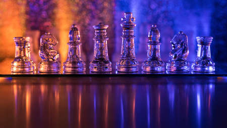 Transparent translucent pieces are placed on chessboard. Concept learning game of chess. Rook Selective Focus. Beautiful orange blue background with reflection for advertising. Tactics and strategyの写真素材