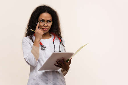 Dark-skinned Physician Holds Blank Ad Space. African American Female Doctor or Scientist in Uniform with Stethoscope looks on Banner on Light Background.の写真素材