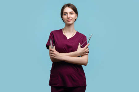 Young Female Surgeon Posing with Steel Surgical Instruments on blue background studio. Woman Doctor Medical Employee wears Medical Uniform Surgical Suit. Concept Training Intern in Practiceの写真素材