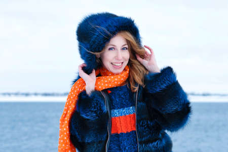 Portrait Girl Walking in Winter Park. Young Woman in Stylish Warm Outfit and Orange Beanie Hat Holds...