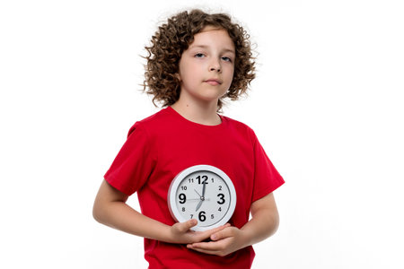 Pleasant curly short-haired female child girl 10-12 years old wears red basic t-shirt. Kind-hearted preteen schoolgirl made heart shape from two palms against chest on white background studio.の写真素材