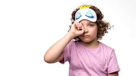 Side view curly short-haired girl 10-12s wears purple basic t-shirt and pink wireless headphones. Female child listening to music, podcast, audiobook on lilac studio background. banner advertisingの写真素材