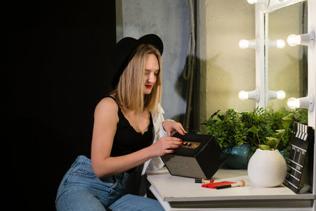 Stylish young beauty woman at dressing room mirror. Lovely girl wears black hat and casual outfit.