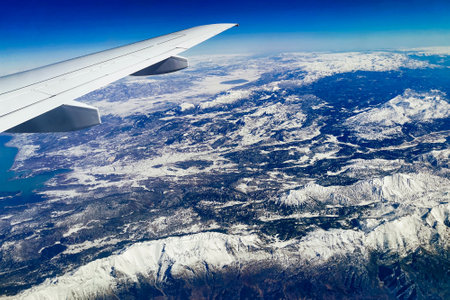 Aerial view through porthole of plane to of snow-covered mountain. Scenic view through aircraft. Airplane. Traveling by air.の写真素材