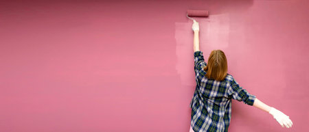 Rear view woman wall and brush painter professionally paint interior wall of apartment with paint roller. Painting apartment, renovation with pink color paint. Bannerの写真素材