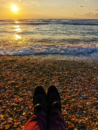 Legs in sneakers of tired tourist at sunset on beach Mediterranean Sea. pov view