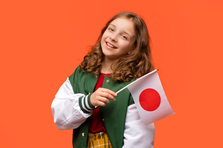 Happy girl wearing in school outfit and holding small national flag of Japan. Teen schoolgirl holds Hinomaruの写真素材