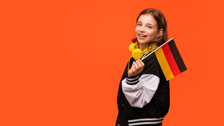 Teen girl in school outfit and yellow earphones holds small flag of Germany. Study abroad and travel. International student exchange program. Learning German, Deutsch.の写真素材