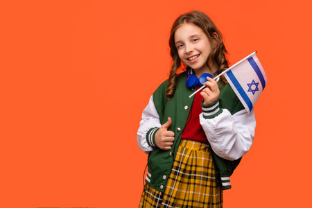 Teen girl in school outfit and blue headphones holds small flag of Israel. Learning Hebrew. Study abroad and travel. International student exchange program.の写真素材