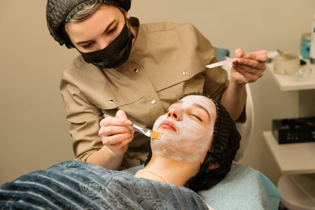 Acne treatment by cosmetician. Esthetician applying cosmetic mask on face teenager girl in beauty salon. Spa treatments, skincare.の写真素材