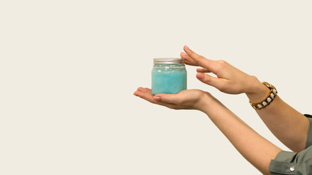 Cosmetician's hands with cosmetic product. Beautician esthetician presenting jar of cream or serum on light background. Empty space for text. Cosmetology and professional skin care.の写真素材