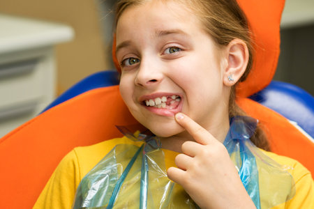 Schoolgirl showing mouth with permanent teeth and lost milk teeth while sitting in dental chair...