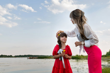 Mom and little daughter are walking by the lake or pond. Mother fixing child's girl hairの写真素材