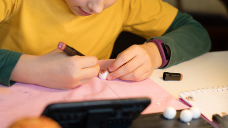 Focused young girl carefully applying detail to a small craft piece, with blurred classroom elements...