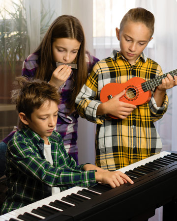 Three kids engage with different instruments, a harmonica, ukulele, and piano, in a cozy roomの写真素材