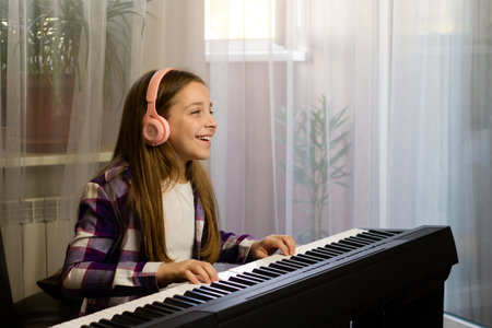 Smiling girl with headphones playing piano at home, enjoying her music practice sessionの写真素材