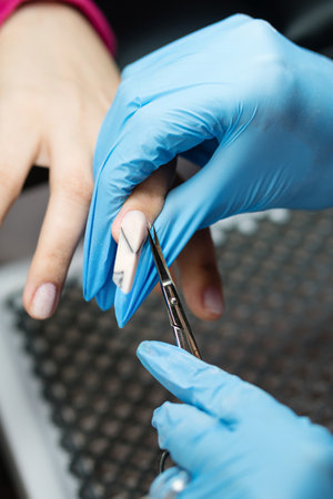 Close-up shot capturing the delicate process of shaping and contouring nails during EDGE manicure. Nail technician in blue gloves uses specialized tools to refine nail's EDGE shape, ensuring sleek and fashionable finishの写真素材