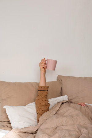 Arm holding coffee mug in bed. Cup held in the hand of a girl in pajamas